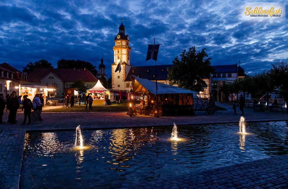 Abendstimmung am Schloss Ehrenstein beim Schlossfest 2025. Man sieht verschiedene Marktstände, die mit Lichtern leuchten.